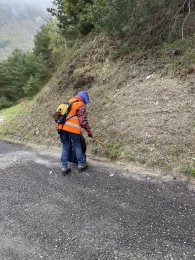 Une personne portant un imperméable ramasse des déchets à l'aide d'une pince et tient un sac poubelle noir à la main.